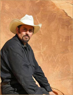 Portrait of Edward K Hudson, Artist and Oil Painter, wearing a cowboy hat, sitting in front of petroglyphs